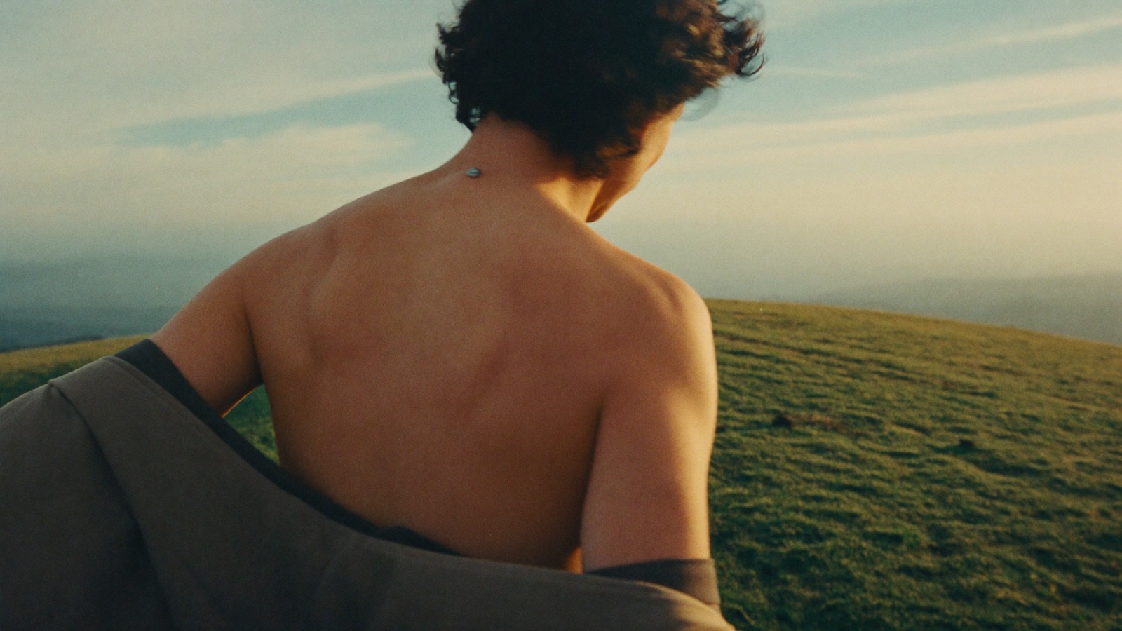 A person on a hilltop at sunrise, shoulders relaxed, breathing out